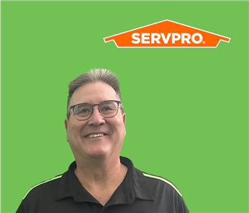 SERVPRO employee with light hair wearing a black shirt in front of a green background