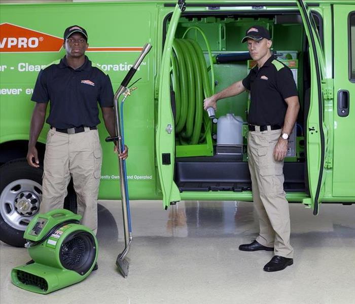 two men standing in front of a green truck, both are holding equipment for water damage