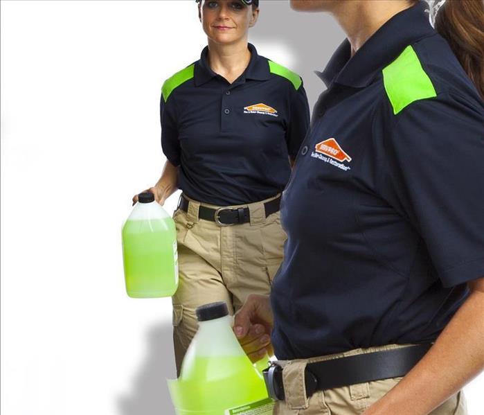 A SERVPRO member carrying a green gallon of a product