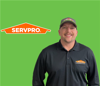 SERVPRO employee with a hat wearing a black shirt in front of a green background